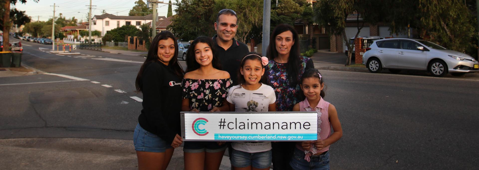 family of 6 standing on corner of two streets holding a street sign