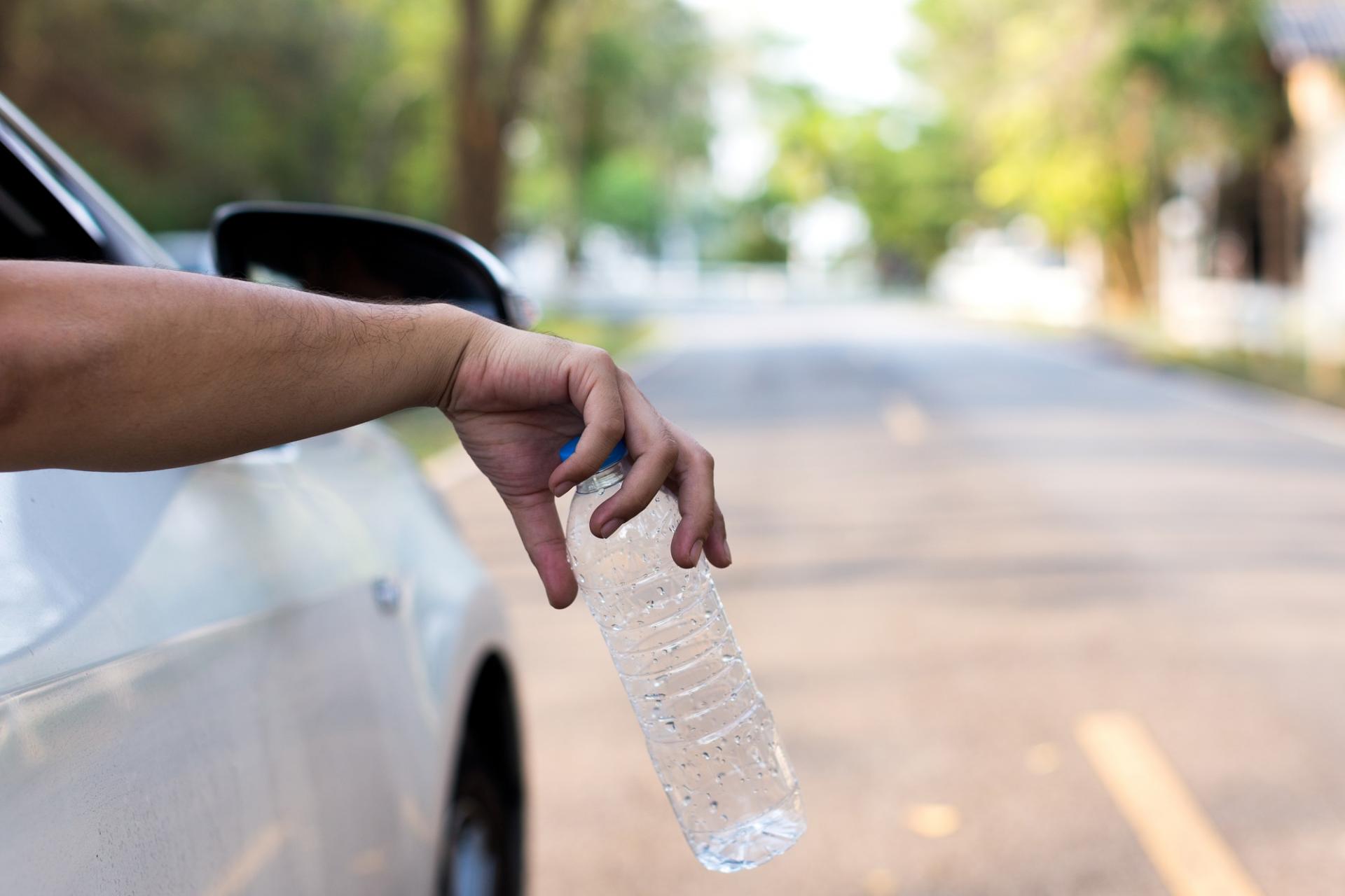 Hand outside car window dropping bottle  on road