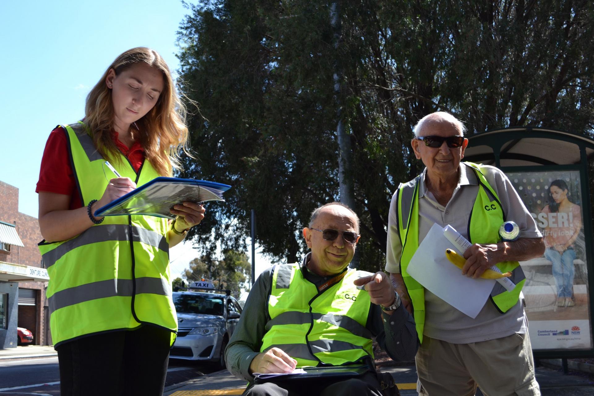 2 men and a women wearing safety vests and writing holding clip boards