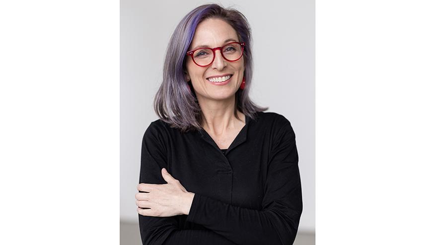Image of Sue Jo Wright, female standing with arms crossed, she has purple hair, red glasses and a black shirt